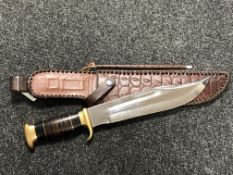 A heavy quality bowie knife with brass mounted grip and stitched leather sheath with sharpener