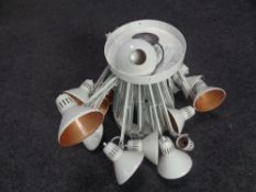 A circular metal light fitting fitted with sixteen angle poise lamps