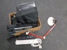 A box containing extension leads, camera tripods, angle poise lamp, laptop bag,