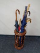 A beech wood stick stand containing a quantity of assorted walking sticks and umbrellas