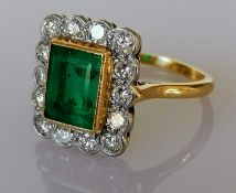 An emerald and diamond cluster ring, milgrain-set in white gold and yellow gold shank: the central