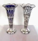 An Edwardian pair of pierced silver vases, one with blue glass liner, each on a stepped base by