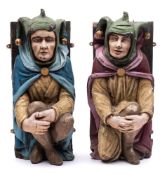 A pair of polychrome carved wood figural corbels of crouching jesters: in traditional costume,