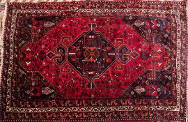 A Kashgai rug:, the brick red field with a central indigo hooked and shaped lozenge medallion,