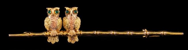 A double owl brooch,: the pair of owls with circular cabochon emerald set eyes, perched on a branch,
