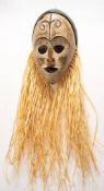 An African,East Nigeria, carved wood and polychrome decorated mask: with raffia tied fringe.