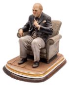A Capo-di-Monte porcelain figure of Winston Churchill: seated in an armchair with cigar in hand,