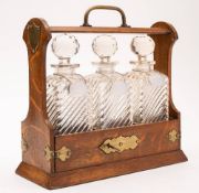 An oak and brass mounted tantalus: containing three clear glass decanters and stoppers with plated
