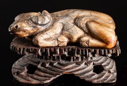 A Chinese carved soapstone model of a reclining bullock: 8cm long, mounted on a wood stand.
