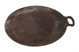 An iron griddle plate or baking iron: with tapered handle, 37cm diameter, another smaller,