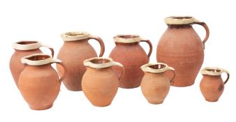 A collection of eight graduated terracotta jugs: with cream slip glazed rims.