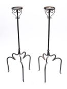 A pair of circular wrought iron candle stands: with turned stems and shaped tripod bases,