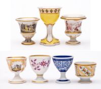 A group of seven egg cups: including a campana-shaped cup painted with a rustic landscape,