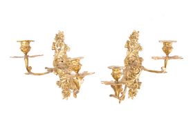 A pair of gilt brass twin branch wall appliques: the urn-shaped sconces mounted on swept foliate