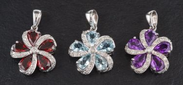 Three 18ct white gold pendants of stylised flowerhead design,: set with garnets,