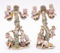 A pair of Dresden porcelain figural four-branch candelabra: modelled as bacchanalian putti around a