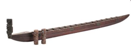 A Maori carved hardwood model of a war canoe: the one-piece hull with carved figurehead and sixteen
