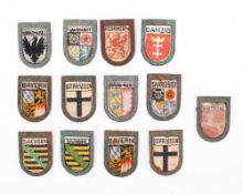 A collection of Third Reich period Winter Helpers Wappen Badges, various towns and districts.