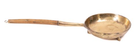 A Bell metal circular frying pan: with turned wood handle, on tripod feet, 23cm diameter.