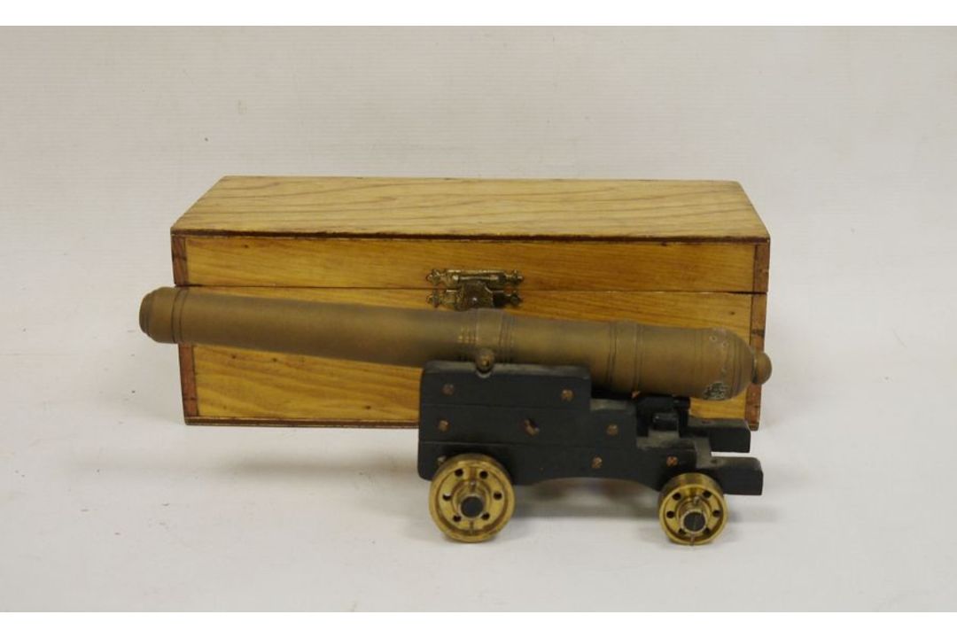 Brass model of a cannon on wooden base with brass wheels, housed in oak case, the barrel approx.