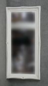 A contemporary bevelled wall mirror in carved and painted frame. H.180 W.84cm
