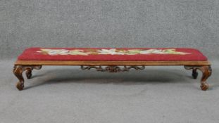 A long walnut hearth stool, with an embroidered insert, over a carved apron of flowers, on scrolling