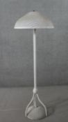 A white painted Lloyd loom wicker standard lamp, with a circular wicker shade, on tripod legs with a