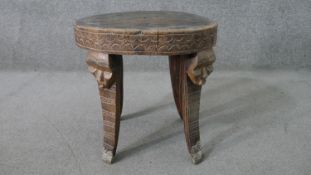 A carved tribal hardwood occasional table, with a circular top, the splayed legs each carved with