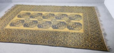 A hand made Afghan carpet with repeating gul medallions on a gold ground contained within multiple