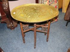 AN EASTERN BRASS TOPPED OCCASIONAL TABLE WITH TYPICAL FOLDING BASE