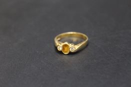 A HALLMARKED 18 CARAT GOLD RING, set with yellow sapphire type central stone and two small diamonds,