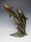 A 20TH CENTURY BRONZED STYLE MODEL OF THREE DOLPHINS AT PLAY, mounted on a naturalistic wave plinth