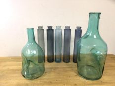 A large glass bottle with indented handle, (43cm h), a similar smaller bottle and five tube shaped