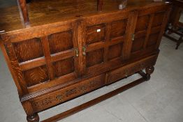A 1950's oak sideboard, in the Jacobean style, having panel cupboards and drawers under on cup and