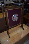 An early 20th Century oak firescreen having woolwork panel