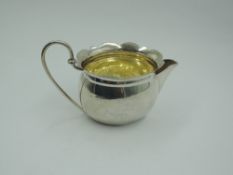 A small Edwardian silver cream jug of oval form having frilled rim, looped wire handle and gilt