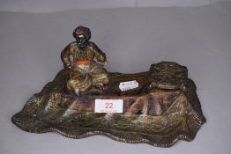 A figural desk top ink well in the form of an Arabian man on carpet in pewter cold painted