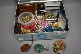 A vintage tin containing a selection of costume jewellery including earrings, brooches, pendants
