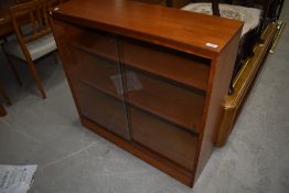 A vintage teak laminate bookcase having sliding glass doors, width approx. 91cm