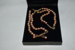 A string of champagne coloured simulated pearls and yellow metal rope chain with matching earrings
