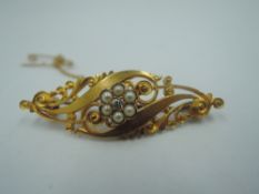 A Victorian 15ct gold brooch having central diamond and seed pearl cluster in an open swirl mount,