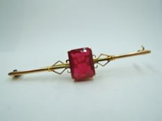 A yellow metal bar brooch stamped 9ct having central facet cut synthetic ruby style stone in claw