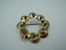 A yellow metal brooch of interlocking circular form having eight inset rubies, no marks, tests as