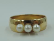A small converted yellow metal wedding band having three attached seed pearls, hallmarks warn, tests