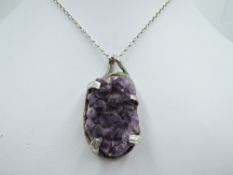 A rough cut oval amethyst pendant in a silver artisan style mount on a white metal chain stamped