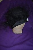 A 1920s silk cloche hat in black with feather decoration.