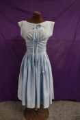 A pale blue 1950s cotton dress having boat neckline with bow detailing, full pleated skirt and