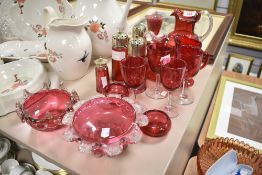 A selection of cranberry glass and a ruby glass jug, amongst the cranberry are sugar sifters,