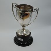 A silver trophy cup having facetted decoration and archectural handles with inscription to front