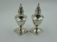 A matched pair of Georgian silver pepper casters of urn form with pierced push on lids and square